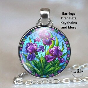 Pode incluir: Pingente redondo prateado com um design de vitral apresentando íris roxas e folhas verdes em um fundo azul. O pingente está em uma corrente de prata. O texto na imagem diz "Earrings Bracelets Keychains and More".