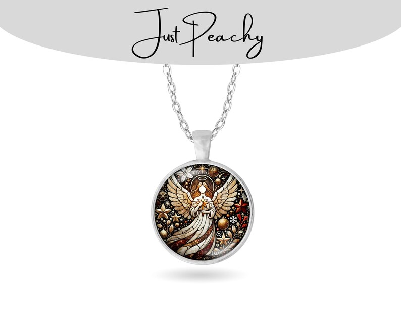 Op de afbeelding: Een zilverkleurige hangerketting met een ronde bedel met een engelontwerp in glas-in-loodstijl. De engel houdt een ster vast, omringd door gouden sterren, rode en witte bloemen en de tekst "Just Peachy".