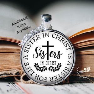 May include: A silver pendant necklace with a round charm. The charm has the text "A SISTER IN CHRIST IS A SISTER FOR LIFE" around the edge. In the center is the word "Sisters" with a cross above it and "IN CHRIST" below. The pendant is on a chain.