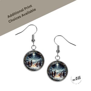 Puede incluir: Un par de pendientes colgantes plateados. Cada pendiente presenta un colgante redondo con una escena invernal que representa un nacimiento con una estrella brillante. El texto "Additional Print Choices Available" es visible.