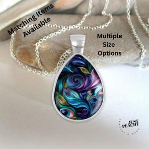 Puede incluir: Collar con colgante plateado con un colgante en forma de lágrima. El colgante presenta un diseño abstracto colorido con remolinos de color turquesa, morado y verde. El texto en la imagen dice "Matching Items Available" y "Multiple Size Options".