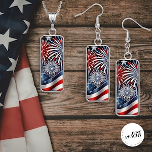 May include: A silver necklace and earrings set featuring rectangular pendants with a patriotic fireworks design. The pendants display red, white, and blue colors, with a star and stripes motif, evoking a festive holiday theme.