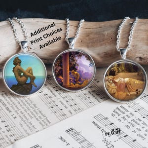 May include: Three silver-toned pendant necklaces with round glass charms featuring classical art prints. The charms hang from delicate chains. The text "Additional Print Choices Available" is visible. The background includes sheet music and a wooden surface.