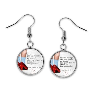 Puede incluir: Pendientes de plata con un fondo blanco redondo que presenta un par de zapatillas de rubí rojas y una cita del Mago de Oz: "Siempre has tenido el poder, mi querida, solo tenías que aprenderlo por ti misma."