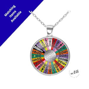 May include: A silver-toned pendant necklace featuring a colorful wheel design with dollar amounts and the words "LOSE A TURN" and "BANKRUPT". The pendant is round and has a chain.