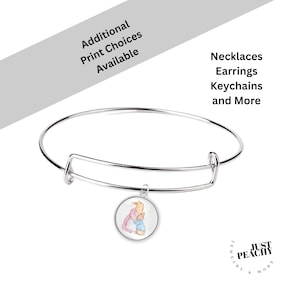 May include: A silver-toned bangle bracelet with a round charm featuring a watercolor illustration of two rabbits. The text "Additional Print Choices Available" and "Necklaces, Earrings, Keychains and More" are also visible.