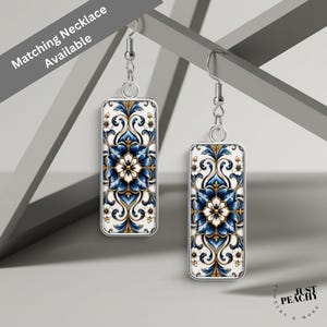 May include: A pair of rectangular drop earrings featuring a silver-tone metal frame and a white, deep blue, and gold floral damask pattern. The earrings hang from silver-tone metal hooks. The text Matching Necklace Available is visible.