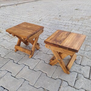 May include: Two wooden folding stools with a natural brown stain finish. The stools are made of solid wood and have a simple, rustic design.