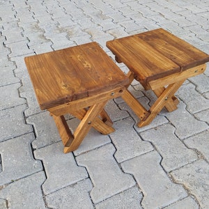 May include: Two wooden folding stools with a brown stain finish. The stools are made of solid wood and have a simple, rustic design.