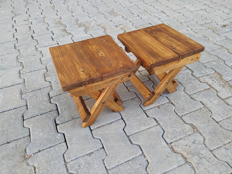 May include: Two wooden folding stools with a brown stain finish. The stools are made of solid wood and have a simple, rustic design.