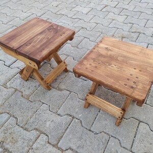 May include: Two wooden folding stools with a natural brown stain. The stools are made of solid wood and have a simple, rustic design.
