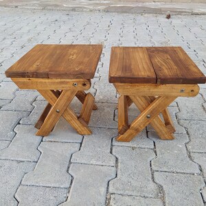 May include: Two wooden folding stools with a natural brown stain finish. The stools are made of solid wood and have a simple, rustic design.