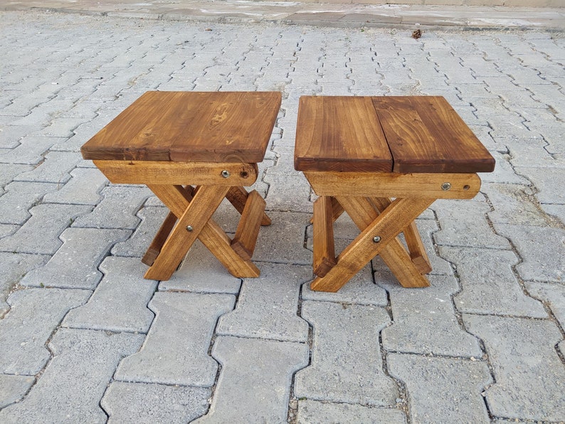 May include: Two wooden folding stools with a natural brown stain finish. The stools are made of solid wood and have a simple, rustic design.