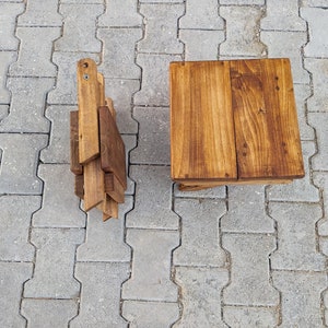 May include: A set of two wooden folding stools. The stools are made of natural wood and have a rustic finish. The stools are folded and stacked on top of each other.