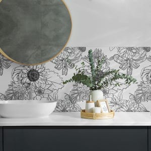 Peut inclure: Une vasque de salle de bain blanche avec un papier peint floral noir et blanc. Un miroir rond est suspendu au-dessus de la vasque. Un vase avec des feuilles vertes et un petit plateau avec des bouteilles et un cadre sont sur le comptoir.
