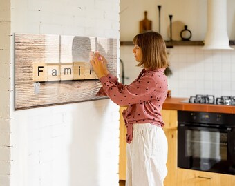 May include: A woman is hanging a wooden sign that says "Family" on a white wall. The sign is made of individual wooden blocks with the letters painted black.