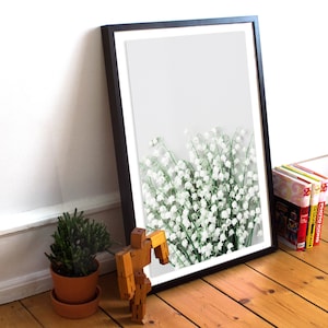 May include: A framed print of a bouquet of white lily of the valley flowers against a light gray background.