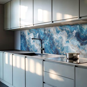 Puede incluir: Una cocina moderna con armarios grises y un salpicadero de mármol azul y dorado. Un grifo negro está montado sobre un fregadero de acero inoxidable. Una placa de cocción negra es visible en primer plano.