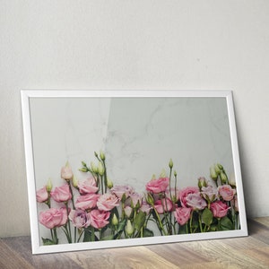 May include: A white frame with a white mat surrounding a photograph of pink flowers against a white marble background.