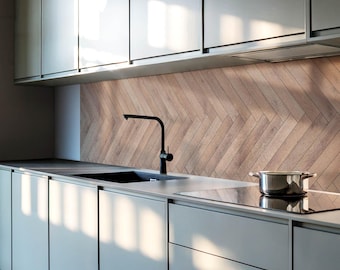 May include: A modern kitchen with gray cabinets and a stainless steel countertop. The backsplash is made of wood tiles in a herringbone pattern. A black faucet is mounted above a stainless steel sink. A pot sits on a black electric stovetop.