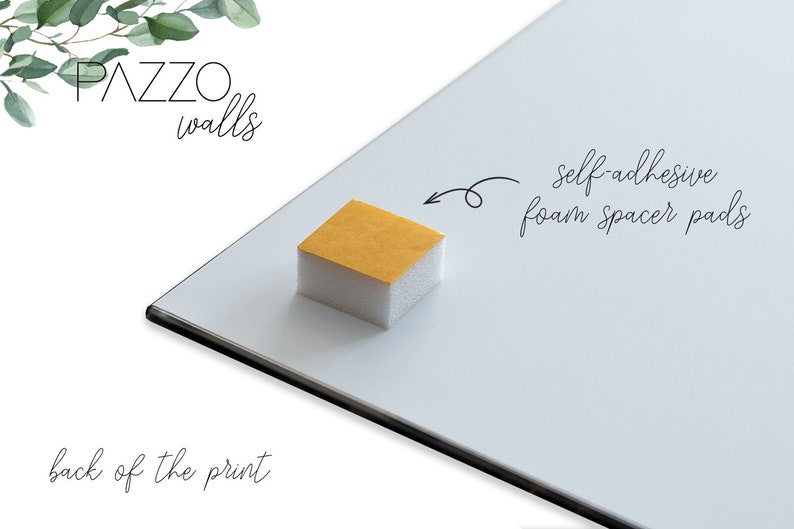 May include: The back of a white framed print with a white foam spacer pad attached. The pad has a yellow adhesive backing and the text "self-adhesive foam spacer pads" is written on the white frame. The text "PAZZO walls" is written at the top of the frame.