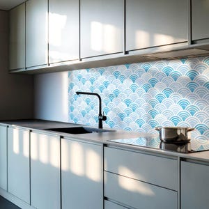 Pode incluir: Uma cozinha moderna com armários brancos e um protetor de parede com padrão azul e branco. Uma torneira preta está montada acima de uma pia de aço inoxidável. Um fogão preto é visível em primeiro plano.