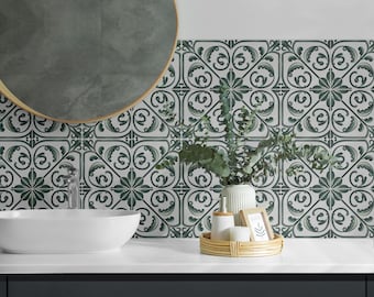 May include: A bathroom vanity with a white ceramic sink and a round mirror with a gold frame. The backsplash is tiled with white and green patterned tiles. A small plant in a white vase and a few bottles are on the counter.
