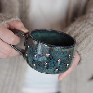 May include: A large, dark blue ceramic mug with a speckled glaze and gold dots. The mug has a rounded shape and a handle.
