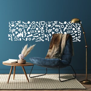 May include: A stylish living room featuring a blue armchair, a small wooden side table, and a brass floor lamp. A wall decal with white abstract shapes is above the chair. A faux fur throw is draped over the chair. A rug and wooden floor complete the scene.