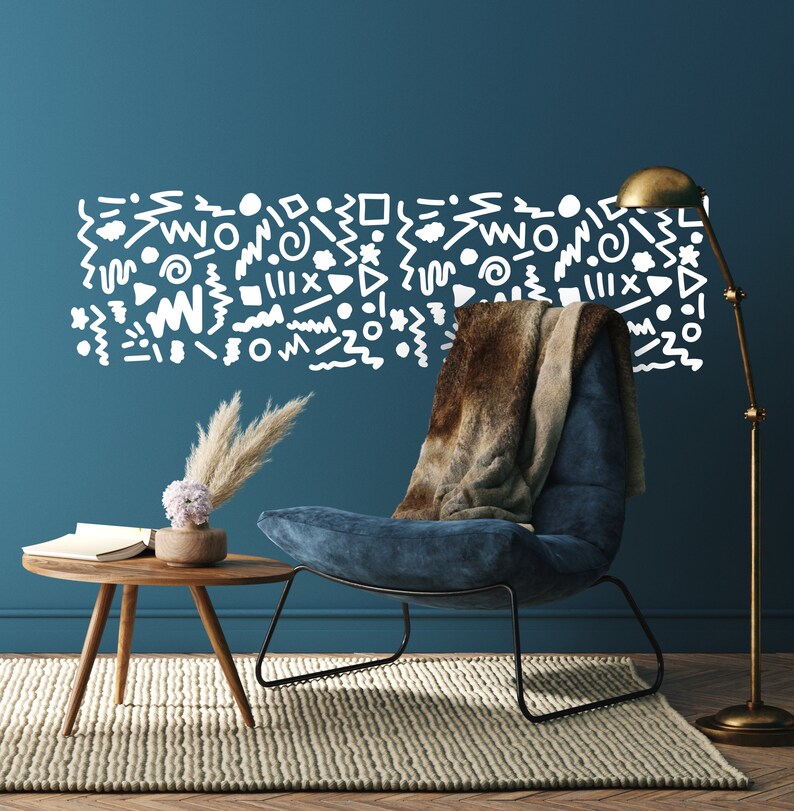 May include: A stylish living room featuring a blue armchair, a small wooden side table, and a brass floor lamp. A wall decal with white abstract shapes is above the chair. A faux fur throw is draped over the chair. A rug and wooden floor complete the scene.
