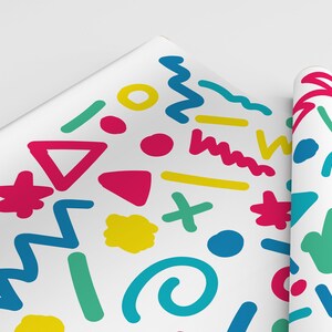 May include: White wrapping paper featuring a vibrant abstract pattern. The design incorporates shapes such as triangles, zigzags, and circles in pink, yellow, green, and blue. A rolled section of the paper is also visible.