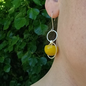 Puede incluir: Un par de pendientes de plata con una cuenta de vidrio amarilla y dos aros de plata.