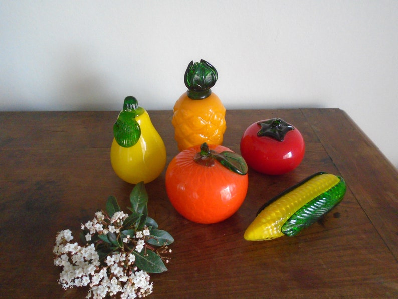 May include: A set of six glass fruit figurines, including a pineapple, pear, orange, tomato, and corn. The figurines are all brightly colored and have a realistic appearance.