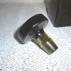 May include: A black glass bottle stopper with a round top and a clear glass neck. The stopper is designed to fit a bottle with a standard neck size.