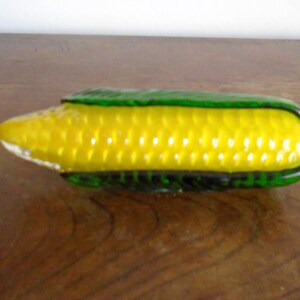 May include: A glass corn on the cob sculpture with a yellow cob and green husk.