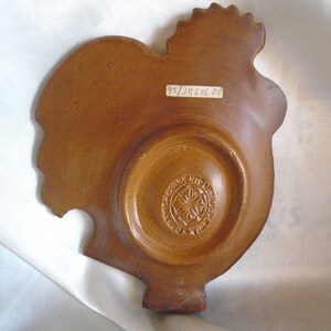 May include: A brown ceramic rooster dish with a decorative design on the bottom. The dish has a label on the back that reads "95/311646 35".