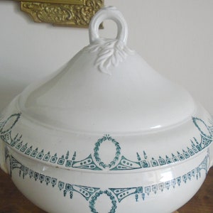 May include: White ceramic serving dish with a lid and green floral design. The dish has a round shape and a decorative handle on the lid.