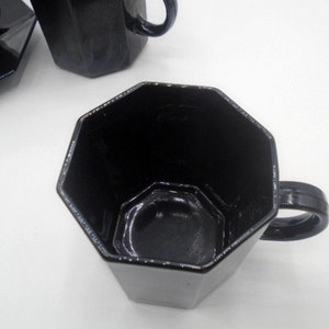 May include: A black octagonal ceramic coffee mug with a handle. The mug is empty and the inside is visible.
