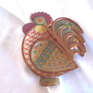 May include: A ceramic rooster figurine with a brown, red, green, and yellow painted design. The rooster has a detailed tail and a raised beak.