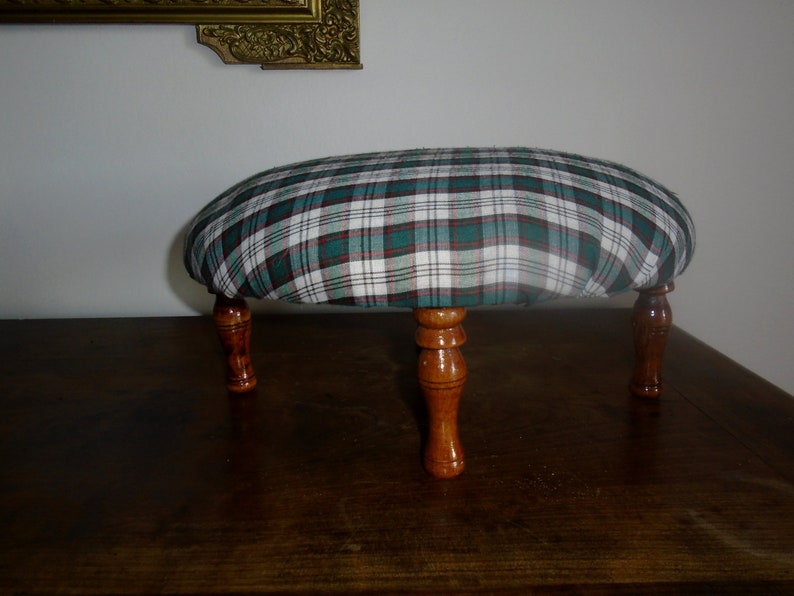 May include: A green, white, and red plaid footstool with four wooden legs.