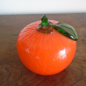 May include: A glass orange with a green glass leaf on top. The orange is a bright orange color and the leaf is a bright green color.