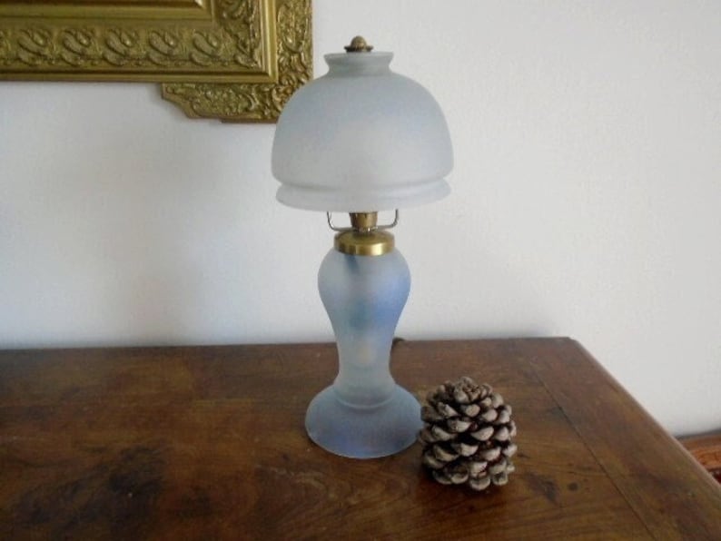 May include: A frosted glass table lamp with a white shade and a blue and white base. The lamp is on a wooden table.
