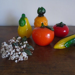 May include: A collection of five glass fruit figurines, including a pineapple, pear, orange, tomato, and corn. The figurines are all brightly colored and have a realistic appearance.