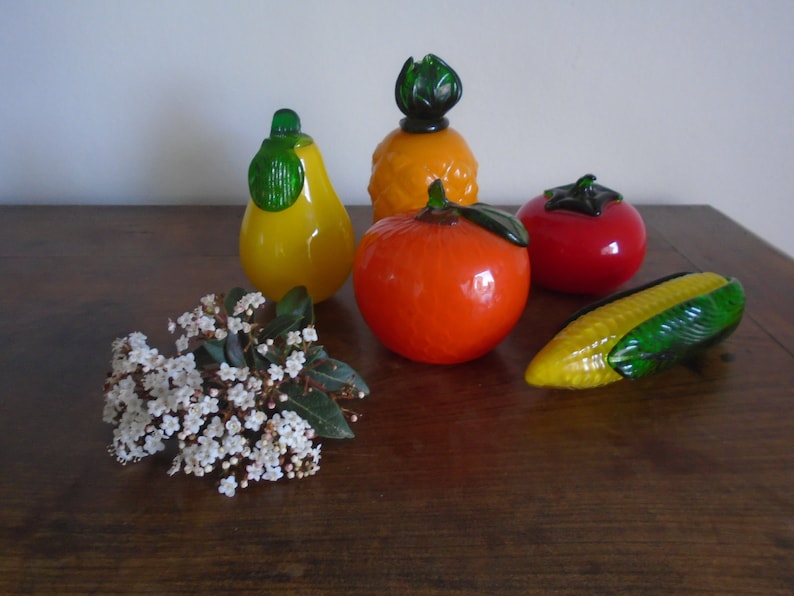 May include: A collection of five glass fruit figurines, including a pineapple, pear, orange, tomato, and corn. The figurines are all brightly colored and have a realistic appearance.