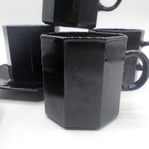 May include: Set of black octagonal glass teacups and saucers. The cups have a unique octagonal shape and a black glossy finish.