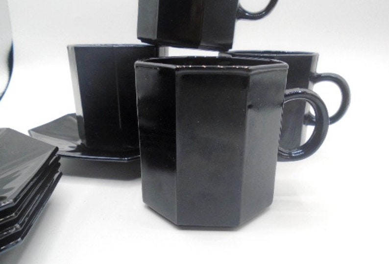 May include: Set of black octagonal glass teacups and saucers. The cups have a unique octagonal shape and a black glossy finish.