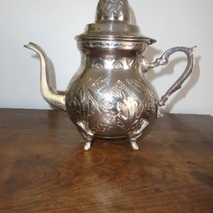 Puede incluir: Una tetera de plata con un dise&ntilde;o ornamentado y una tapa. La tetera tiene un pico y una manija y se apoya en tres patas.