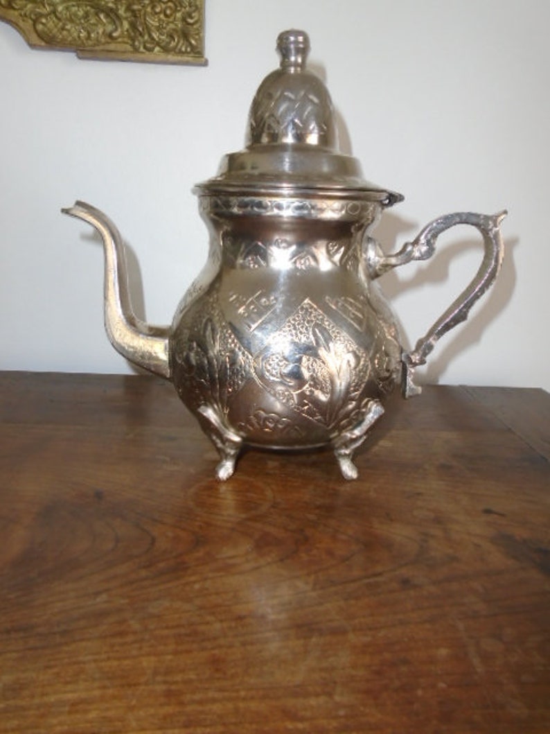Puede incluir: Una tetera de plata con un dise&ntilde;o ornamentado y una tapa. La tetera tiene un pico y una manija y se apoya en tres patas.