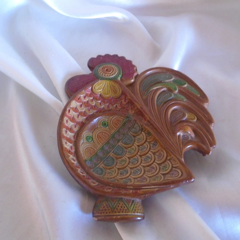 May include: A ceramic rooster dish with intricate details. The rooster is painted in shades of brown, orange, green, and yellow. The dish has a scalloped edge and a raised base.