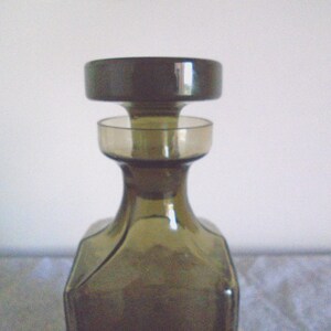 May include: A dark green glass bottle with a wide mouth and a removable stopper. The bottle has a square base and a rounded body.